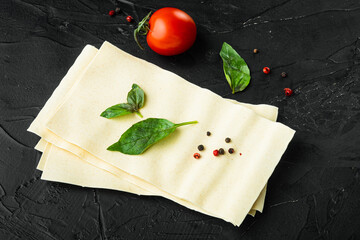 Organic lasagna pasta sheets, with seasoning and herb, on black stone background