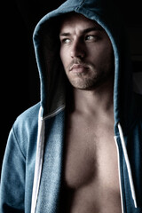 Handsome young man standing next to window with blue eyes, open hoodie revealing defined pecs