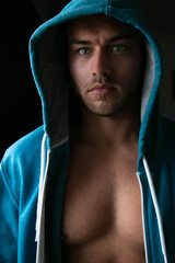 Portrait of handsome young man standing next to window with blue eyes, open hoodie revealing...