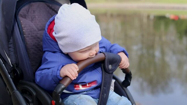 Cute little boy licks handle from pram while walking in park