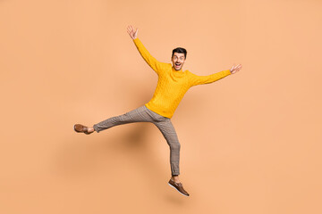 Full length photo portrait of excited guy spreading arms legs like star jumping up isolated on pastel beige colored background