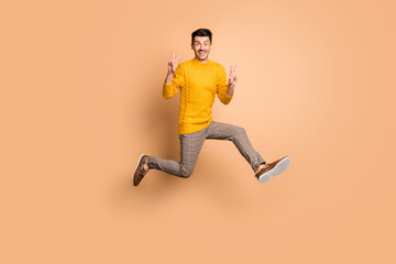 Fototapeta na wymiar Full length photo portrait of funny man making two v-signs jumping up isolated on pastel beige colored background