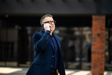 Senior businessman walking and having a conversation at phone. Portrait of mature confident smiling man wearing elegant suit walking on the street and talking phone.