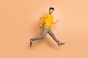 Fototapeta na wymiar Full length photo portrait side profile of man running jumping up isolated on pastel beige colored background