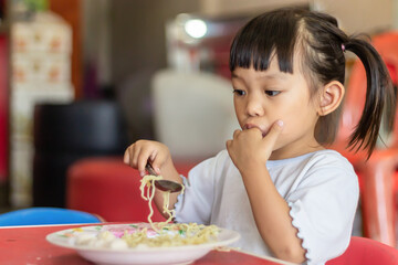 Portrait​ image​ of​ 2-3 yeas​ old​ of​ baby.​ Happy​ Asian child girl eating and biting the noodle. Enjoy eating moment. Healthy food and kid concept.​ Sucking fingers in the mouth.