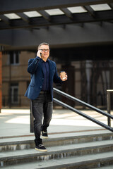Mature handsome businessman taking phone sitting at outdoor with Coffee cup on the street