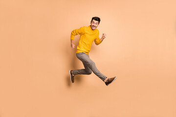 Fototapeta na wymiar Full length photo portrait side profile of cheerful guy running jumping up isolated on pastel beige colored background