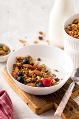Homemade granola with nuts, berries, seeds and milk in white plate on table for healthy breakfast