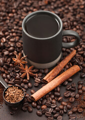 Black coffee in tall cup with anise star and cinnamon on ground coffee and beans with coffee scoop