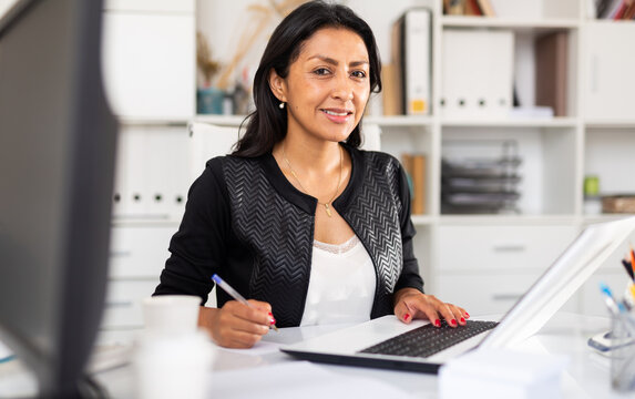 Smiling successful hispanic business woman working on laptop in modern office