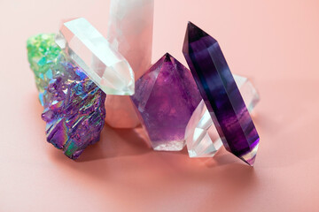 Various crystals for healing and magical practices. Faceted amethyst, rose quartz, fluorite, rock crystal, a cluster of quartz on a pastel pink background