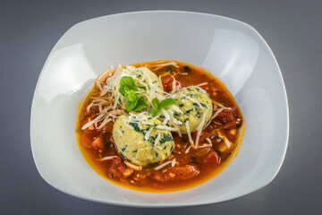 Homemade traditional Italian spinach and cheese ricotta malfatti with tomato sauce garnished with grated parmesan cheese and basil leaves on grey background