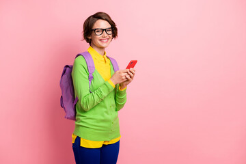 Photo of cute young lady dressed yellow shirt glasses backpack holding modern device empty space isolated pink color background