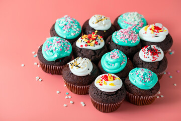 Chocolate cupcakes with turquoise and white icing and sugar shaped sprinkles. Sweet holiday food close-up on pink background
