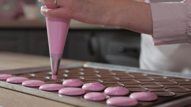 Chef Pastry Chef Confectioner Makes Macarons In The Kitchen, Piping Out Pink Mixture Dough on Slip Mat for Baking Macarons Shells in Kitchen of Pastry Shop, Copy Space, Close Up 