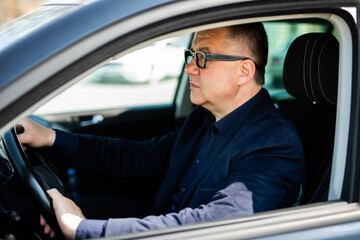 Fototapeta na wymiar Handsome middle-aged man driving a modern car on the street