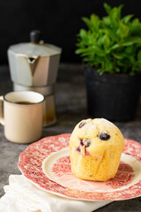 Blueberry muffins on a grey and black background. Coffee maker in the back, with a cup and a plant of mint