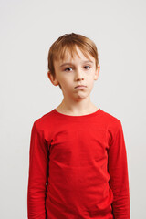 Portrait of sad boy standing against white wall. Unhappy kid looking to the camera. Face emotions and expression. © volurol