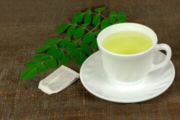 Moringa Tea in white cup and fresh green leaf on brown wooden background. Moringa oleifera tropical herb healthy lifestyle concept.