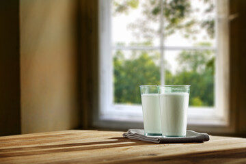 Two glasses full of milk. Wooden table with shadows and a napkin. home interior with a large window in the morning. Place for your product or inscription. 