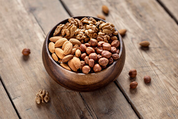 Various nuts in wooden bowl on wooden background close up, copy space