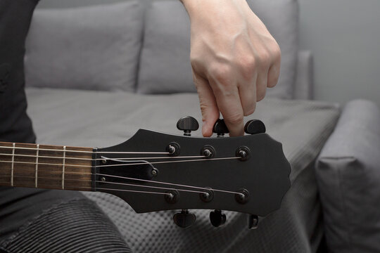 Black electric guitar tuning. Fingers are turning the tuning peg. Hand in the frame. Learning to play the guitar.