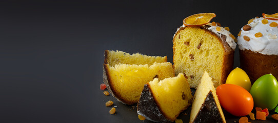 Traditional Easter cake on dark black background. Migdal, candied fruits, raisins, decor colorful eggs. wide Sectional view, slices, pieces. Orthodox treat. Copy space