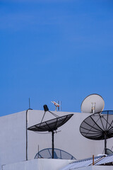 3 satellite dishes with tv antenna on top of the old gray building against blue clear sky background in vertical frame