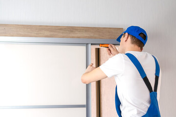 Handyman who installs sliding doors at home in overalls with a screwdriver in his hands repairs the door