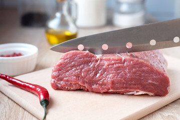 A knife is cut raw veal fillet on a cutting board in the kitchen, cooking at home.