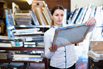 Satisfied pleasant girl is choosing modern picture in furniture store.