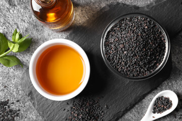 Black sesame seeds and oil on grey table, flat lay
