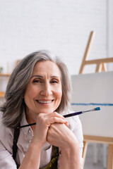 joyful middle aged painter with grey hair holding paintbrush