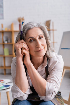 pleased middle aged painter with grey hair holding paintbrush