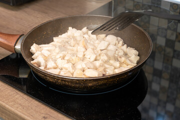 In a frying pan, pieces of chicken meat are fried on an induction stove close-up