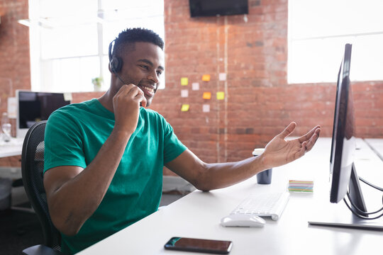 African american businessman having video call sitting in front of computer using headphones - Powered by Adobe