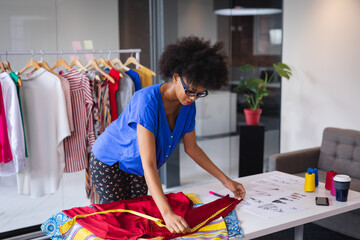 Mixed race fashion designer working in office measuring clothes on table with clothes in background