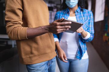 Diverse male and female colleagues at work discussing and looking at tablet wearing face masks