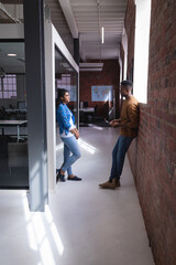 Diverse male and female colleagues at work standing discussing in corridor