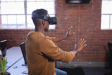 African american man in office wearing virtual reality set and playing