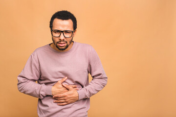 Young handsome african american black man with hand on stomach because indigestion, painful illness feeling unwell. Ache concept. Isolated over beige background.