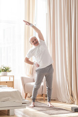 Senior bald man in yoga side stretch asana doing exercies alone at home.