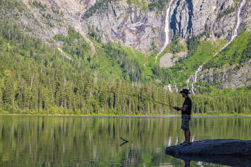 Fototapeta na wymiar Fisherman showing off his catch at Avalanche Lake and surrounding mountain range at Glacier National Park