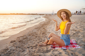 young happy crazy attractive caucasian woman freelancer, wearing a hat, sitting on a sandy beach by the sea with a laptop on her laptop