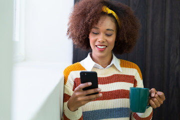 Portrait of mixed race businesswoman using smartphone and holding coffee mug