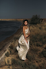 A beautiful girl in a stilted suit stands on a mountain above the sea, a lake on a sunny day.