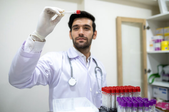 Man Doctor Or Specialist In Lab Coat Wearing Glove And Looking At Test Tube Sample In The Clinic. There Are Many Tube Sample In The Rack On The Tray. Laboratory, Testing And Lifestyle Concept.
