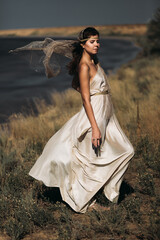 A beautiful girl in a stilted suit stands on a mountain above the sea, a lake on a sunny day.