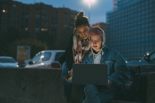 Two young caucasian women outdoor at night using computer