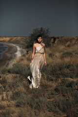 A beautiful girl in a stilted suit stands on a mountain above the sea, a lake on a sunny day.